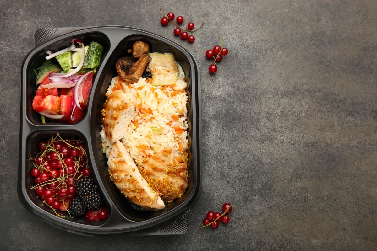 Packaging meal in lunch box on a black background. Top view, copy space.